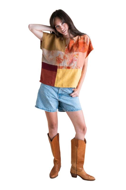 Woman wearing a colorful patchwork top and denim shorts with brown boots on a beige background